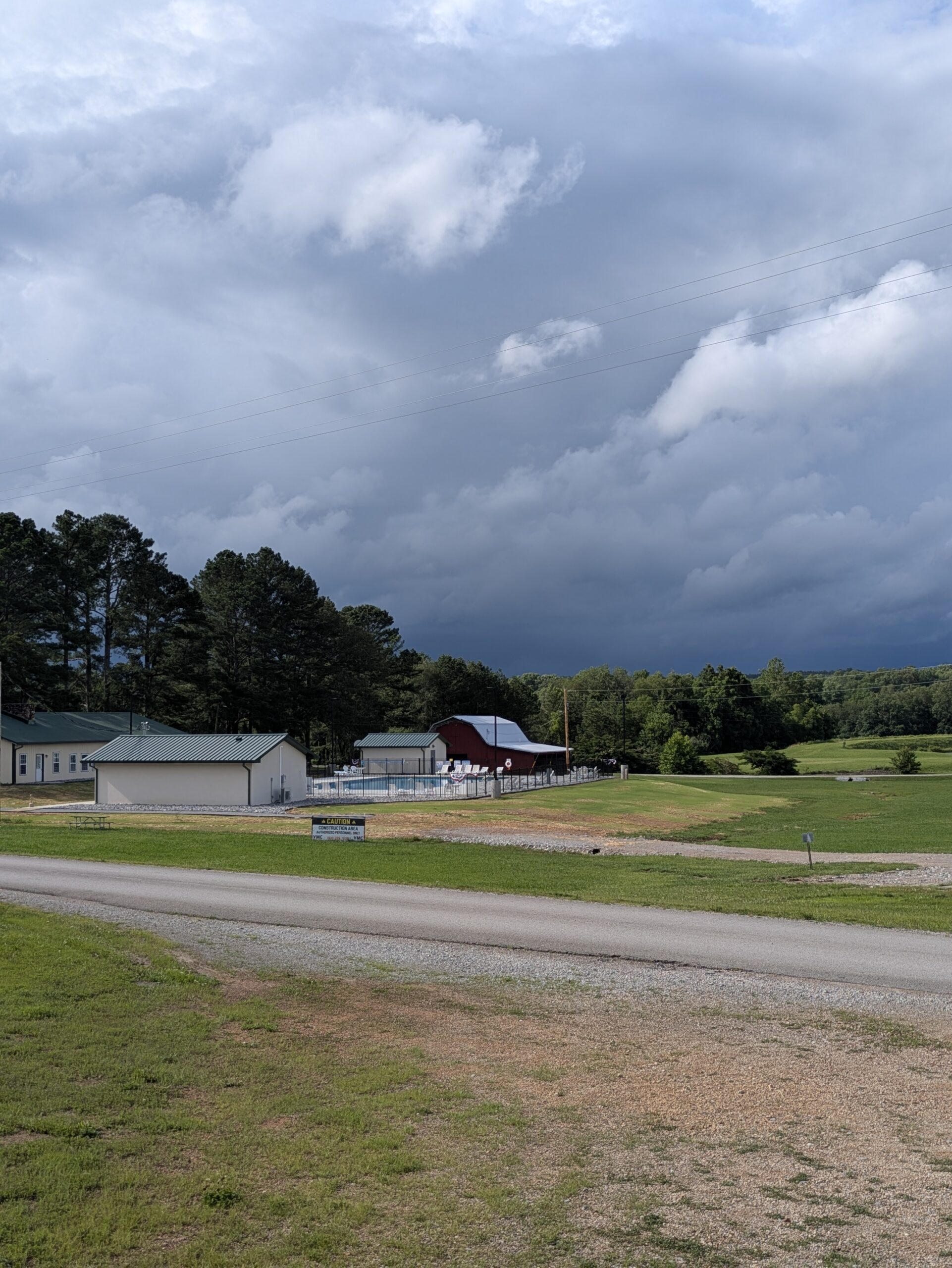 Newly constructed pool and bathhouse at Natchez Trace Campground in Hohenwald, TN, built by VMC Facilities, featuring a fenced pool area, pool equipment building, and surrounding open green landscape under a cloudy sky.