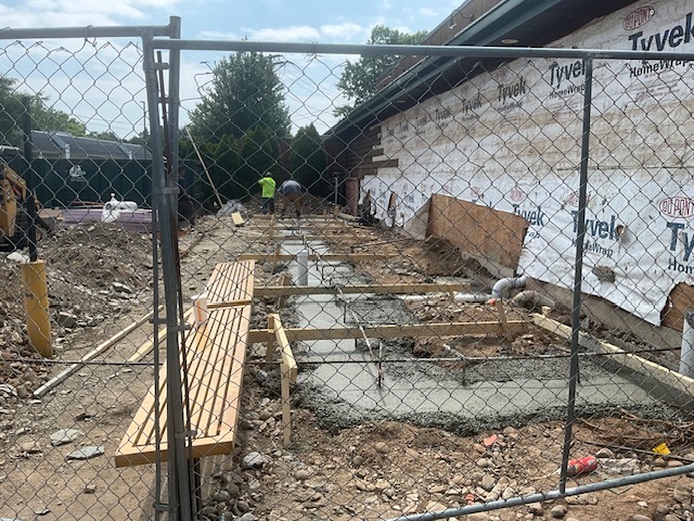 Concrete foundation being poured and leveled for cooler addition at rear of Texas Roadhouse in West Haven, CT, with Tyvek-wrapped exterior wall and workers on site.