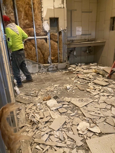 Restroom demolition in progress during restaurant renovation showing exposed wall insulation and broken tile on floor