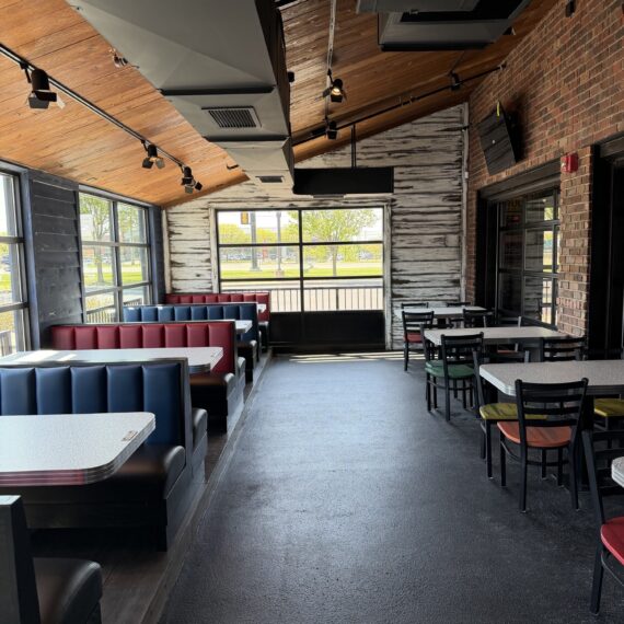 Completed restaurant dining room addition in Sterling Heights, Michigan featuring custom red and blue booth seating, wood plank ceilings, exposed brick walls, industrial lighting, and modern restaurant interior finishes.