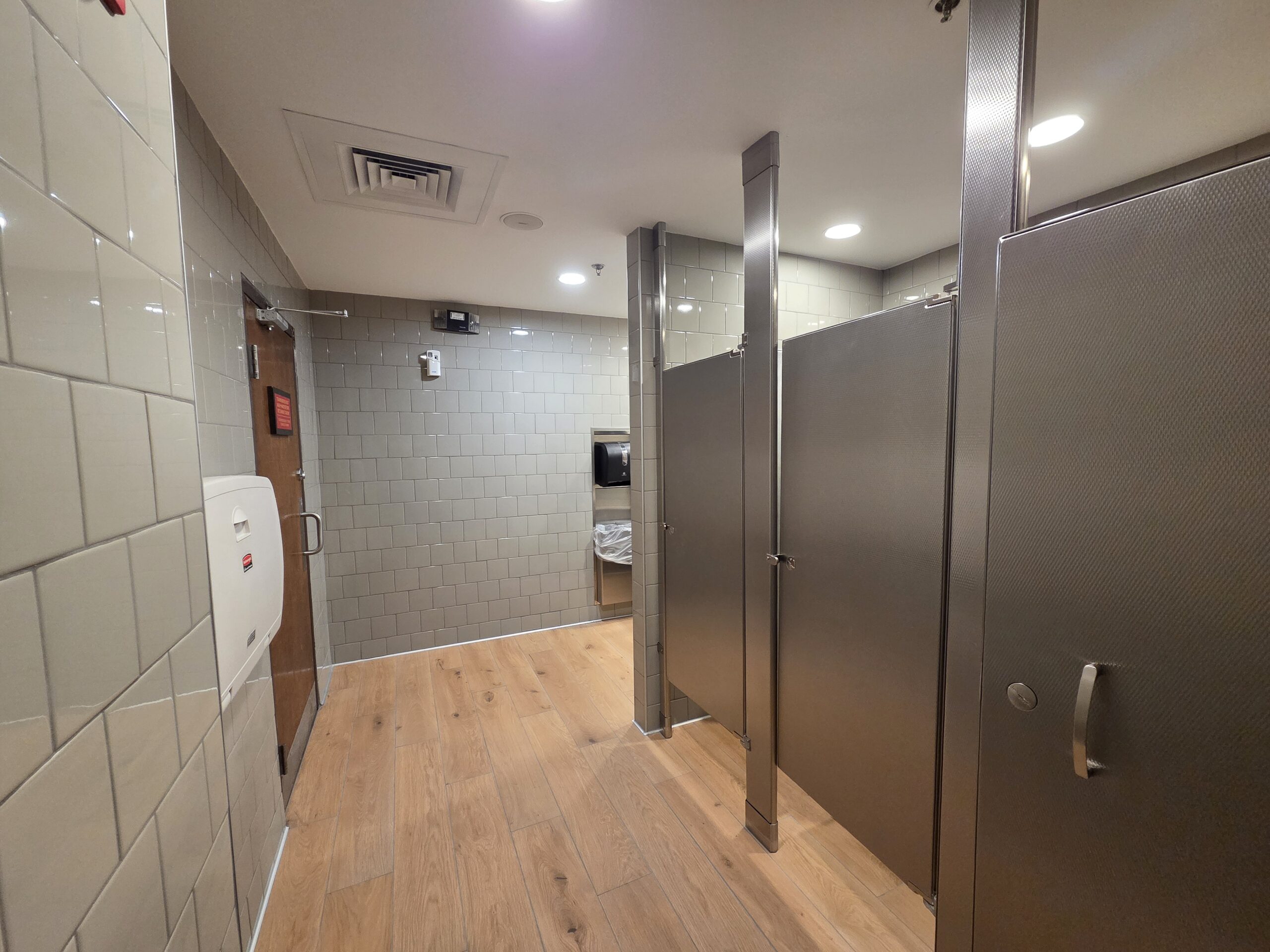 Renovated Chili’s restaurant restroom in Virginia Beach VA featuring modern subway tile walls, wood-look porcelain flooring, stainless steel partitions, ADA-compliant fixtures, and updated commercial sinks.