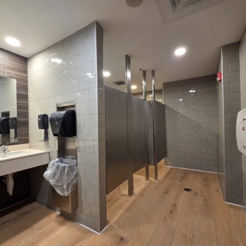 Renovated Chili’s restaurant restroom in Virginia Beach VA featuring modern subway tile walls, wood-look porcelain flooring, stainless steel partitions, ADA-compliant fixtures, and updated commercial sinks.