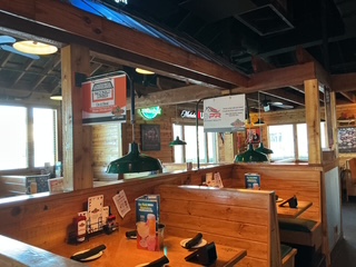 Interior view of the completed front-of-house remodel at Texas Roadhouse in Fayetteville, North Carolina, featuring refreshed wood booths, decorative corrugated metal wall panels, updated lighting, timber columns, and the restaurant's signature rustic Western design.